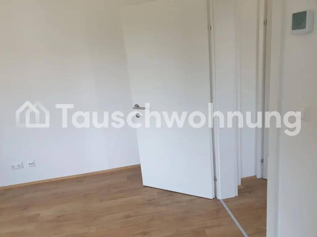 Leerer Raum mit weiß gestrichenen Wänden, Holzboden und einer modernen Tür.