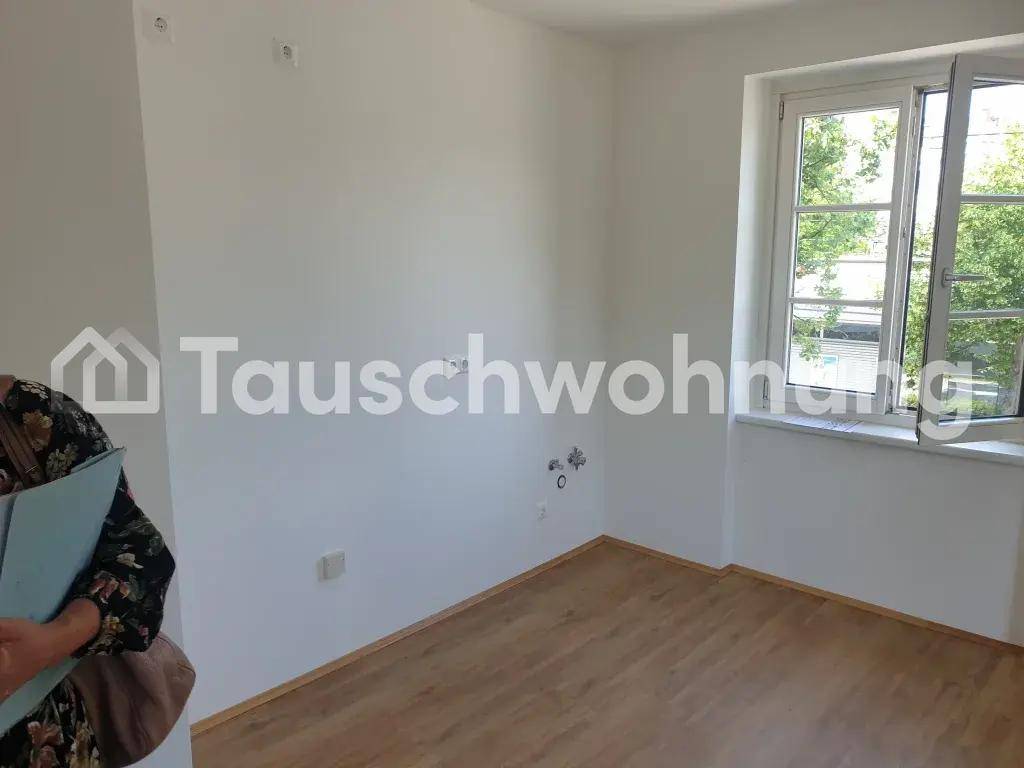 Leeres Zimmer mit einem großen Fenster, das den Blick ins Grüne freigibt, und Laminatboden.