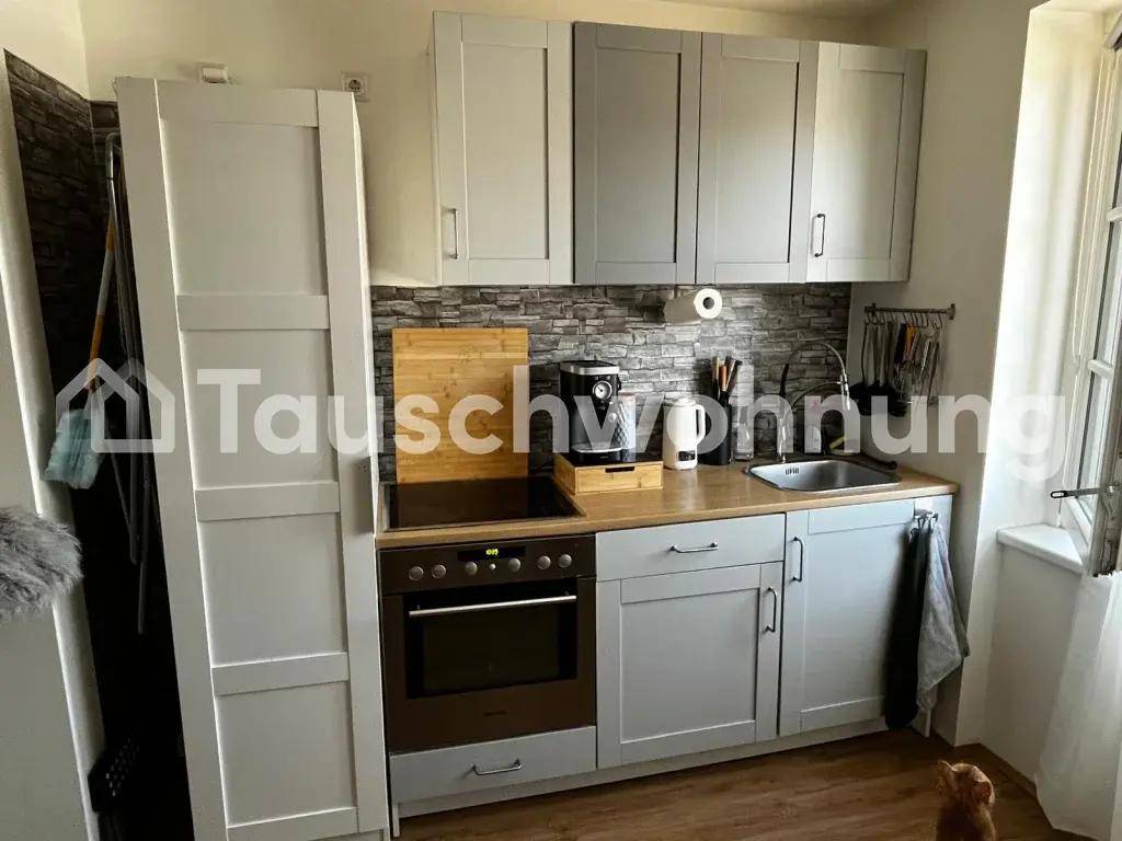 Kleine, moderne Küche mit hellgrauen Schränken, Holzarbeitsplatte und integriertem Backofen.