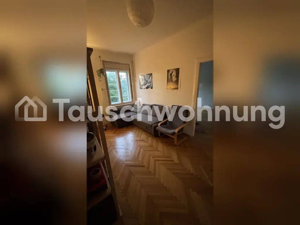 Gemütliches Wohnzimmer mit Sofa, Fischgrätparkett und einem Fenster, das Tageslicht hereinlässt.