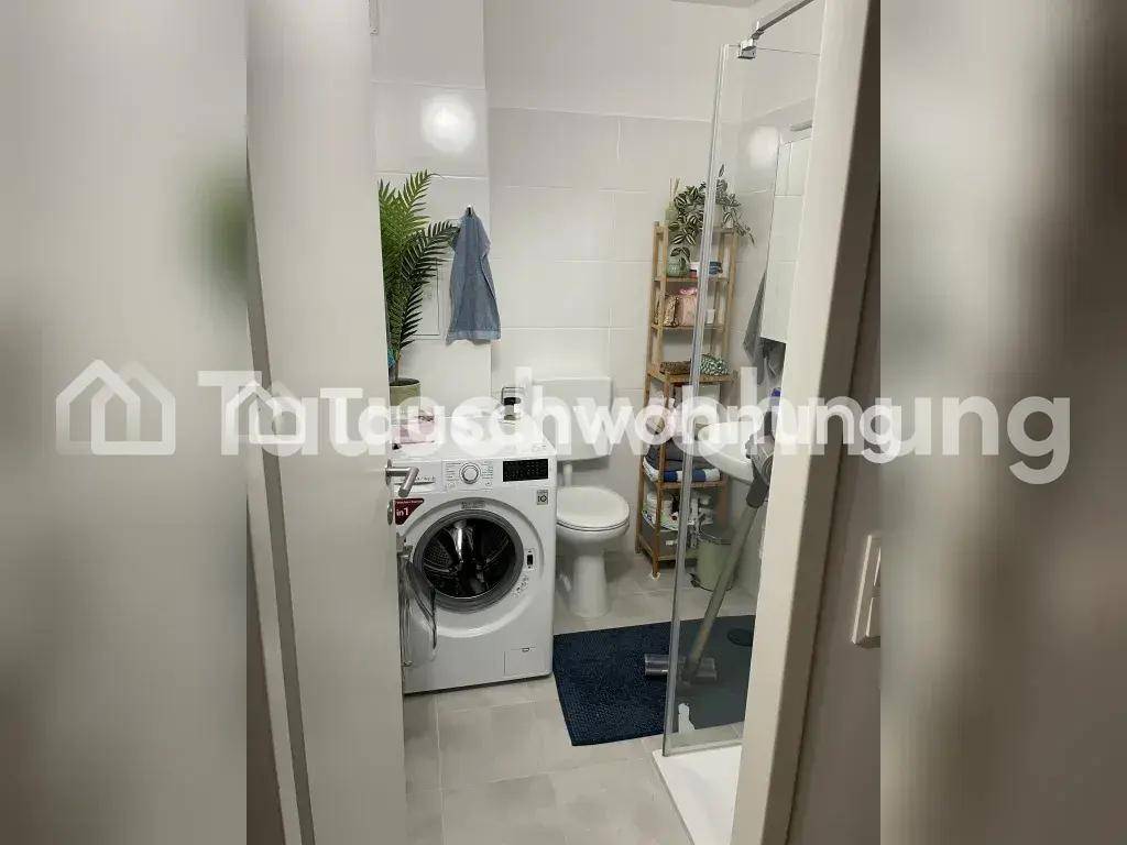 Modernes Badezimmer mit Dusche, WC und Waschmaschine, hell gefliest.