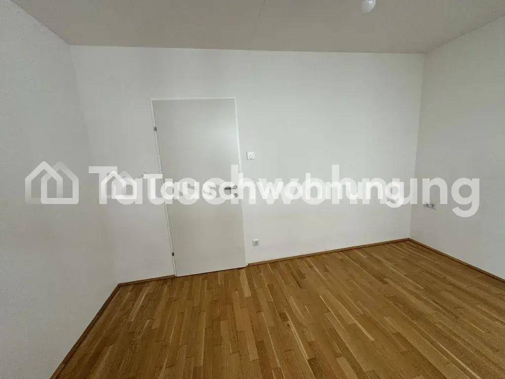 Heller, leerer Raum mit Holzboden und einer Tür, die zu einem weiteren Bereich führt.