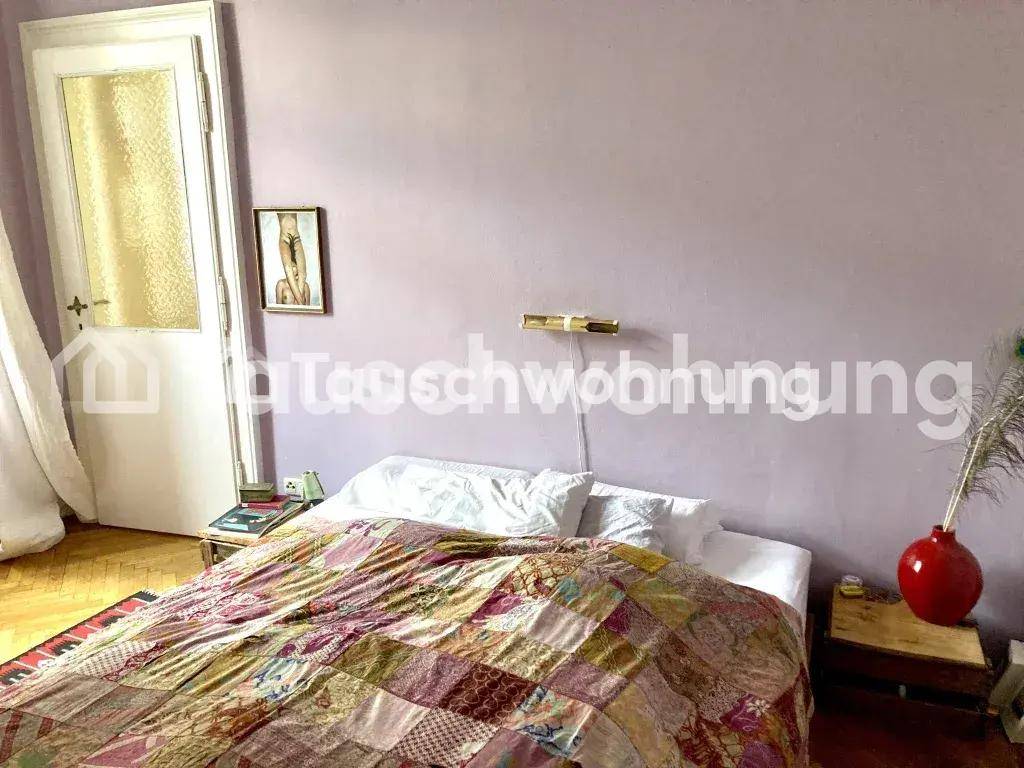 Schlafzimmer mit einem gemütlichen Bett, farbenfroher Tagesdecke und hellvioletten Wänden.