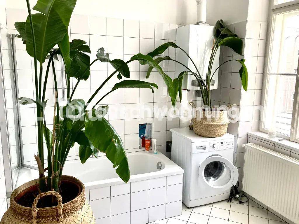 Badezimmer mit weißen Fliesen, Badewanne, Waschmaschine und einem Fenster für natürliche Belüftung.