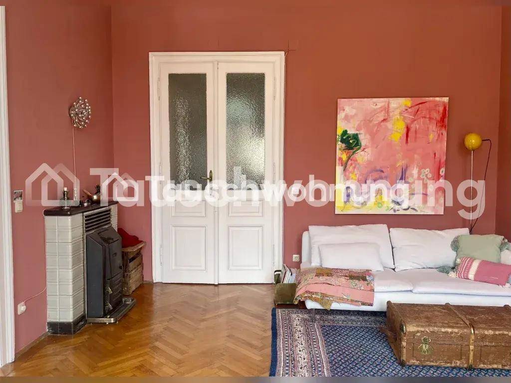 Wohnzimmer mit Sofa, Fischgrätparkett, rosa Wänden und einem traditionellen Kachelofen.
