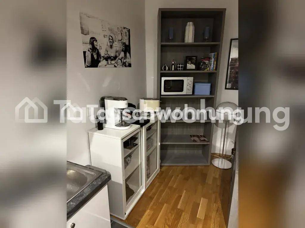 Kleine Küchenzeile mit Spüle, Kaffeemaschine, Mikrowelle und hohem Regal.