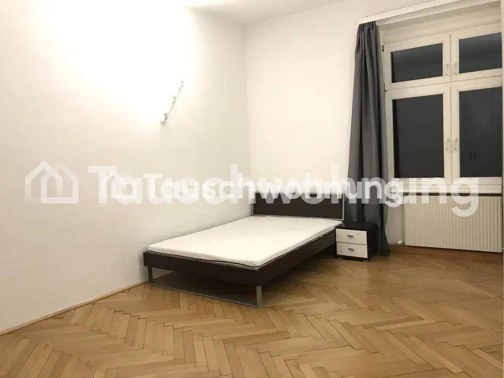 Helles Schlafzimmer mit Doppelbett, Nachttisch, großem Fenster und Fischgrätparkettboden.