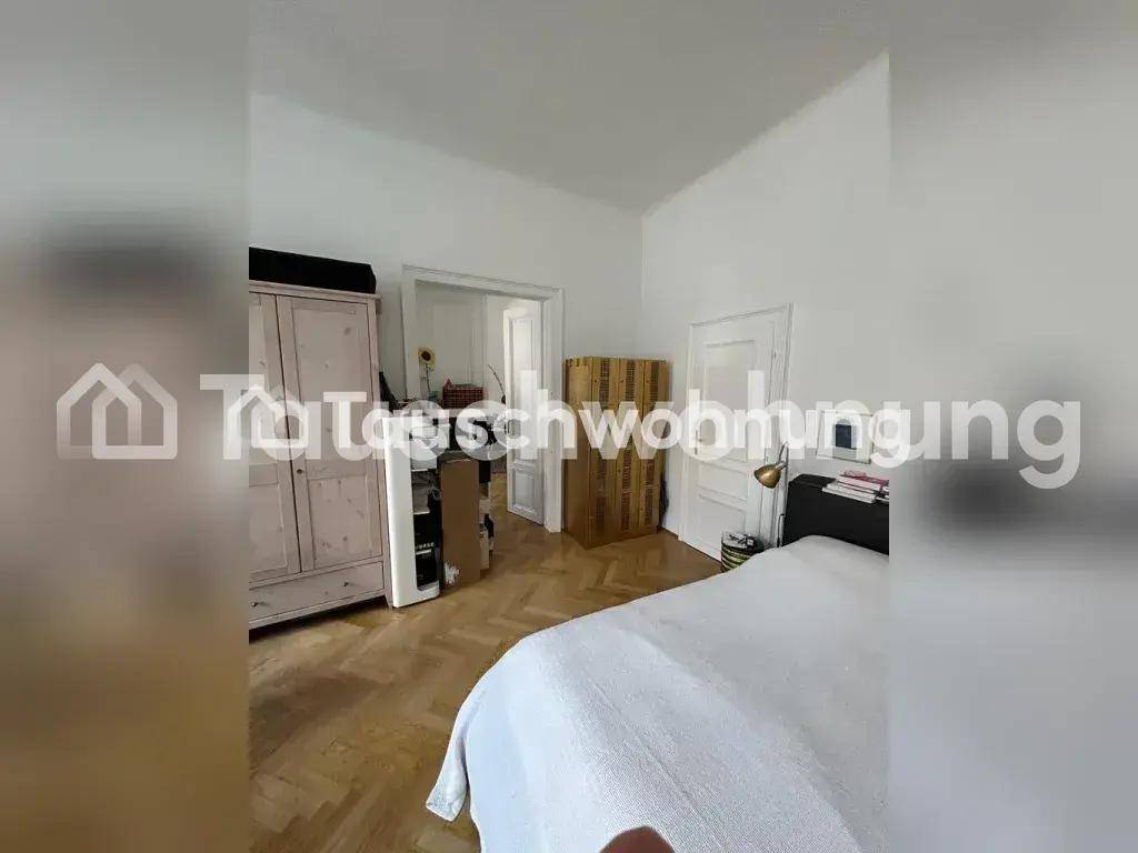Schlafzimmer mit Fischgrätparkett, großem Kleiderschrank und Bett, mit Zugang zu einem weiteren Raum.