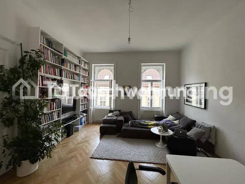 Geräumiges Wohnzimmer mit Bücherregal, Sofa und Fischgrätparkett, hell durch große Fenster.