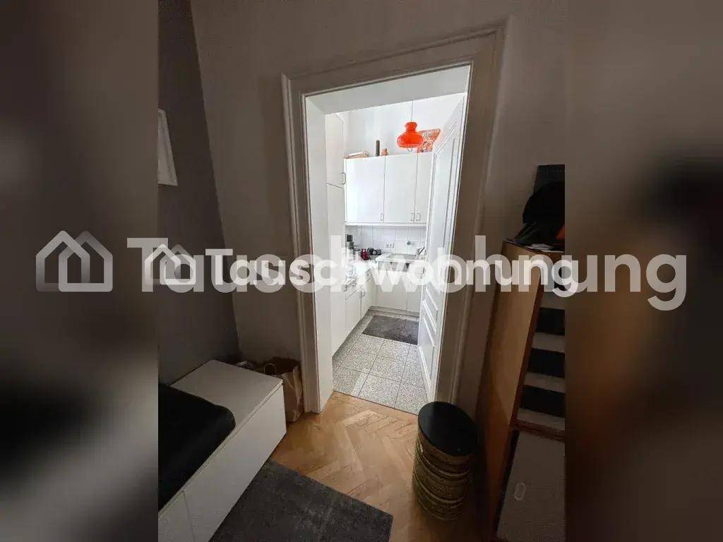 Blick durch eine Tür in eine kleine Küche mit weißen Schränken und Fliesenboden.