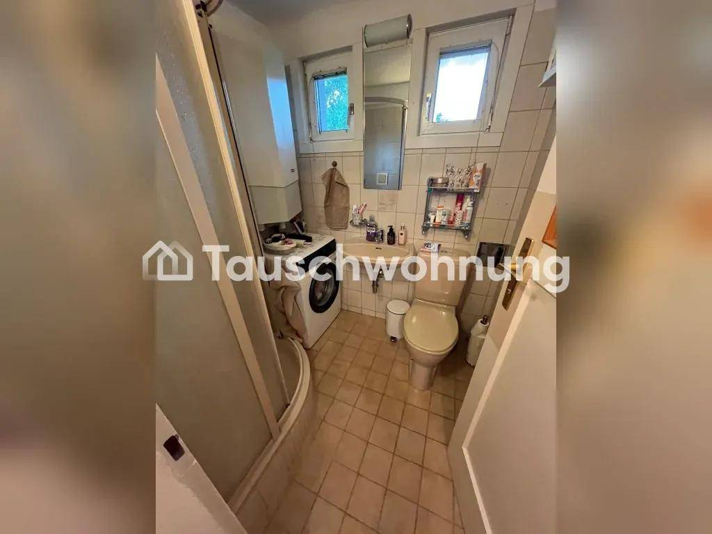 Kleines Badezimmer mit Dusche, Toilette, Waschmaschine und Fenster.