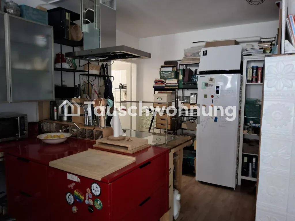 Funktionale Küche mit roten Schränken, großem Kühlschrank und einer Kochinsel in einem belebten Raum.
