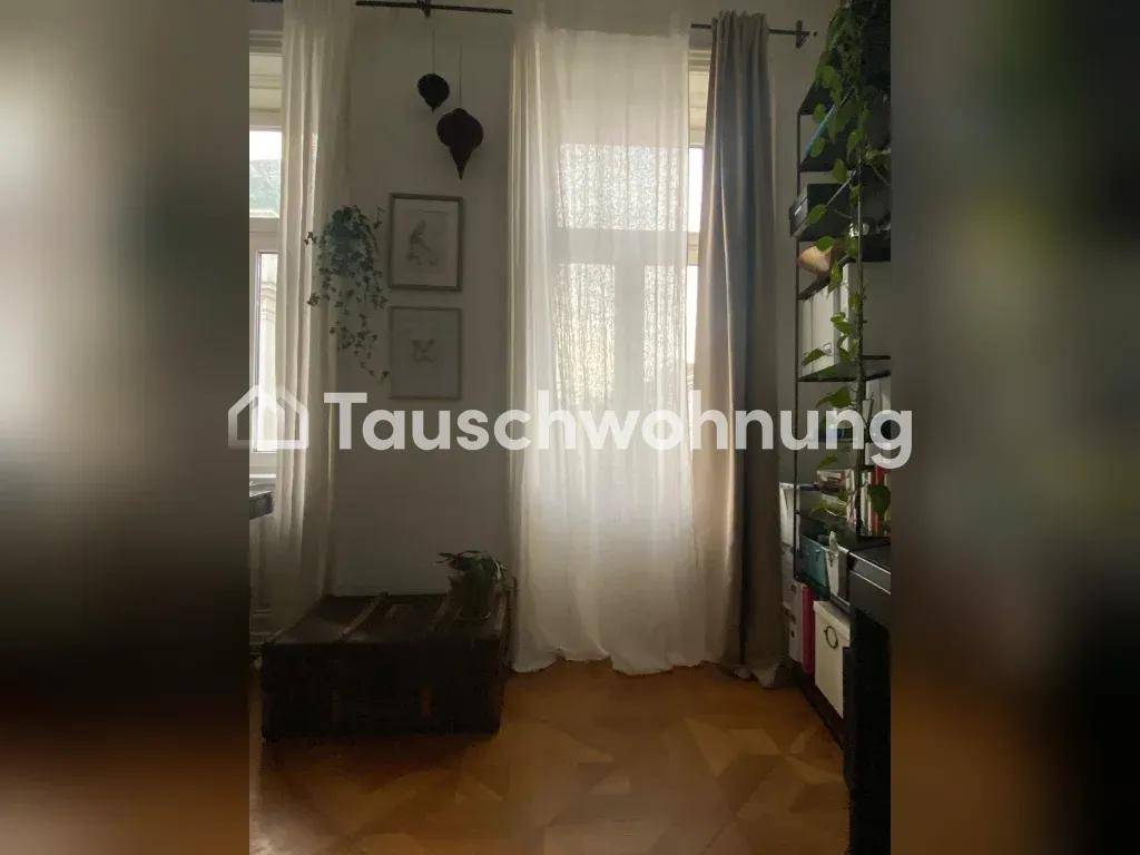 Helles Zimmer mit hohen Fenstern, Vorhängen und einem Bücherregal.