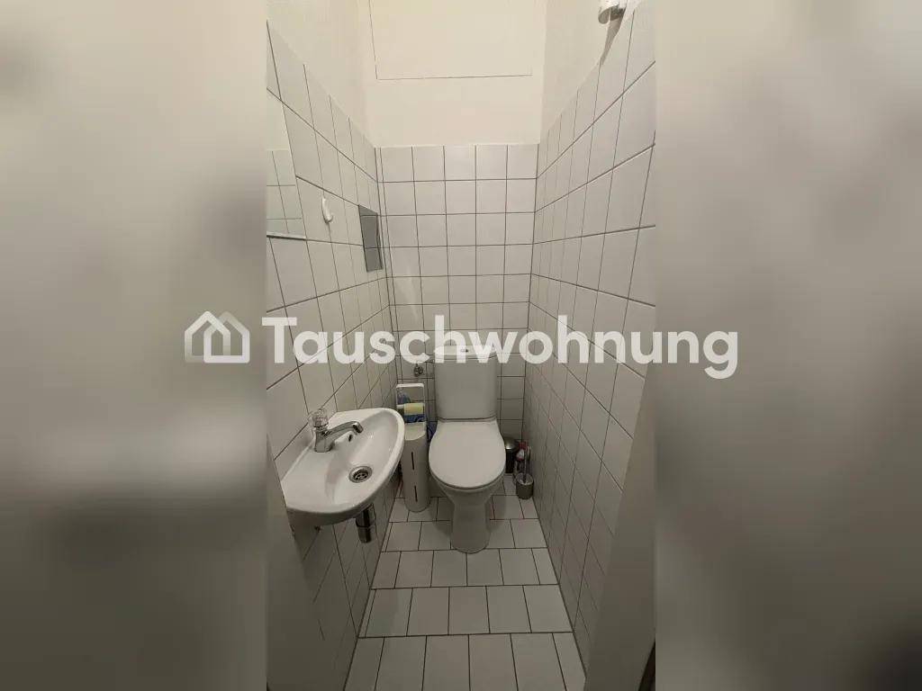 Separates WC mit Toilette, kleinem Waschbecken und weißen Fliesen an Wänden und Boden.