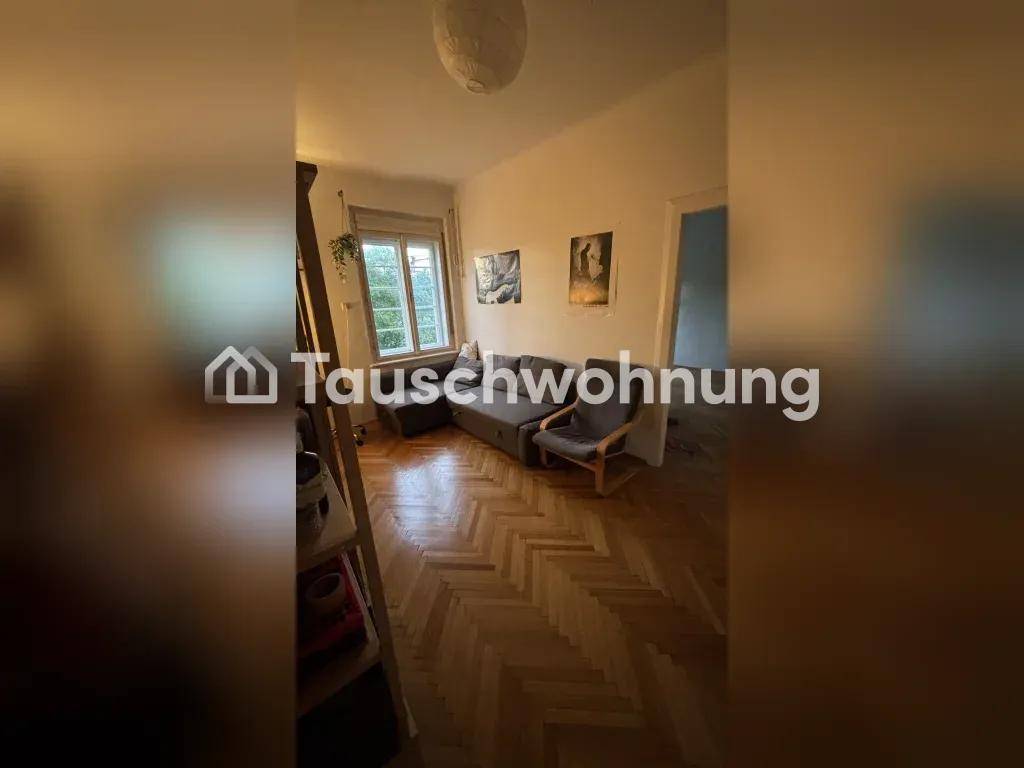Gemütliches Wohnzimmer mit Sofa, Sessel, Fischgrätparkett und einem Fenster.