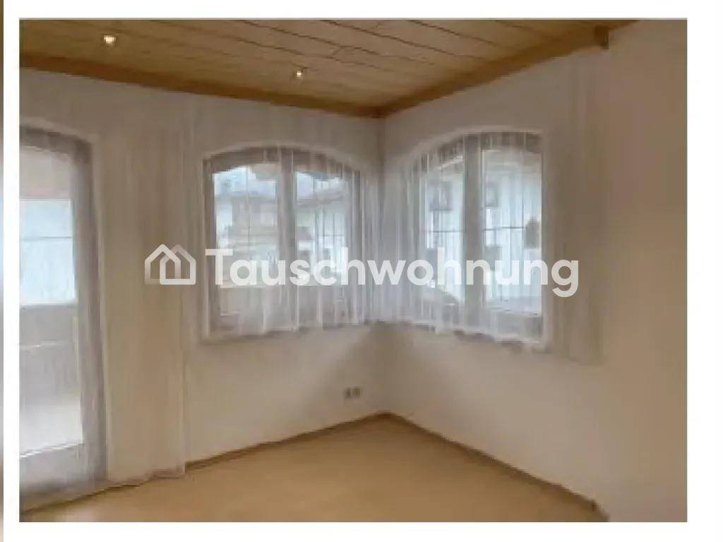 Heller Wohnraum mit Holzbalkendecke, zwei Rundbogenfenstern und Zugang zum Balkon.