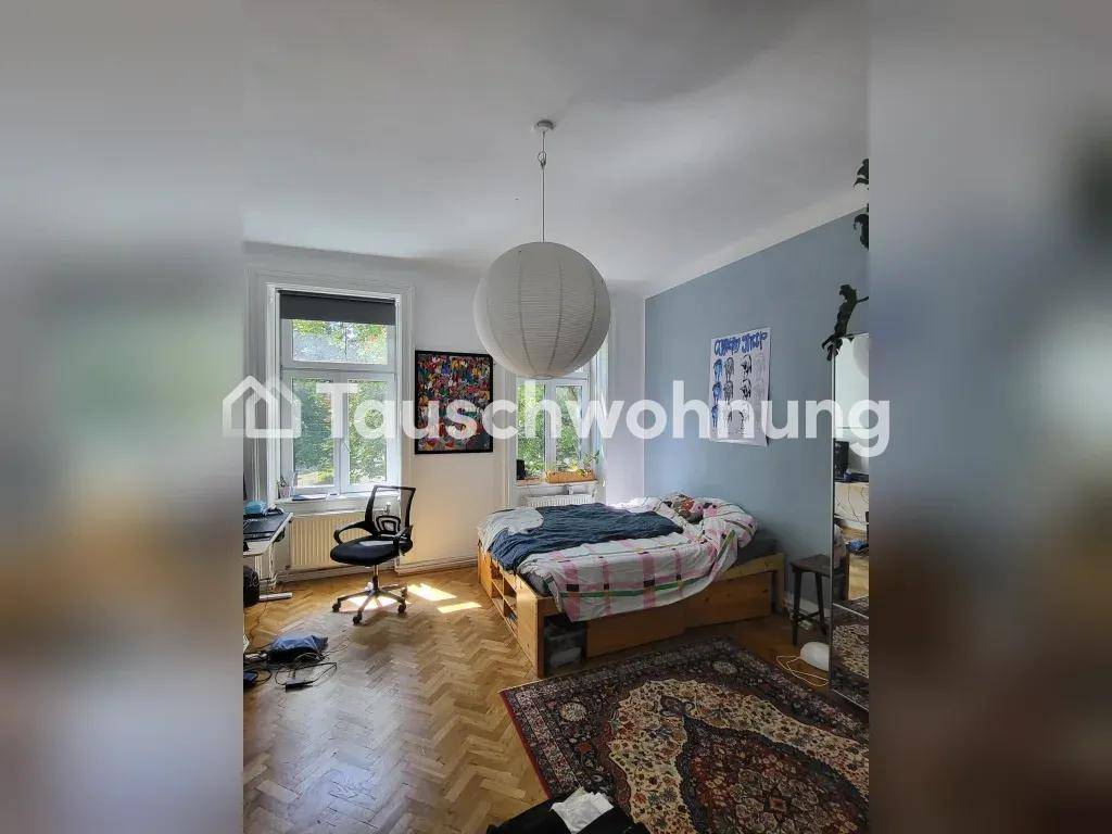Schlafzimmer mit Holzbett, Schreibtisch und Fischgrätparkett, hell durch großes Fenster.