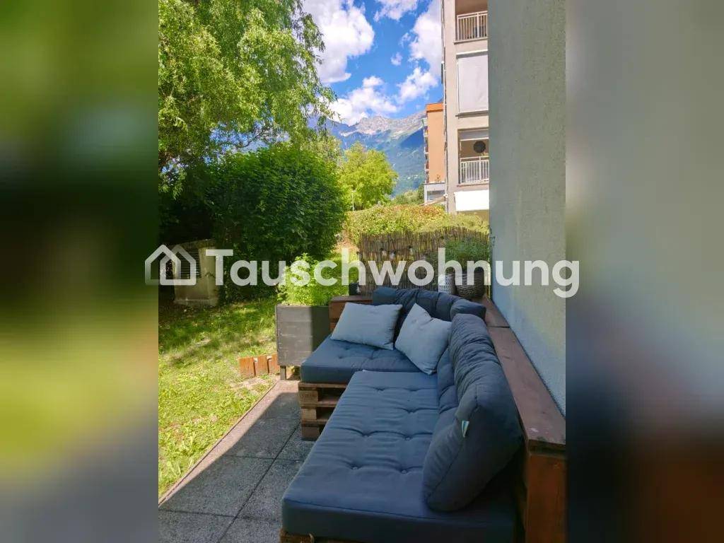 Terrasse mit Palettensofa und Blick auf grüne Bäume und Berge im Hintergrund.
