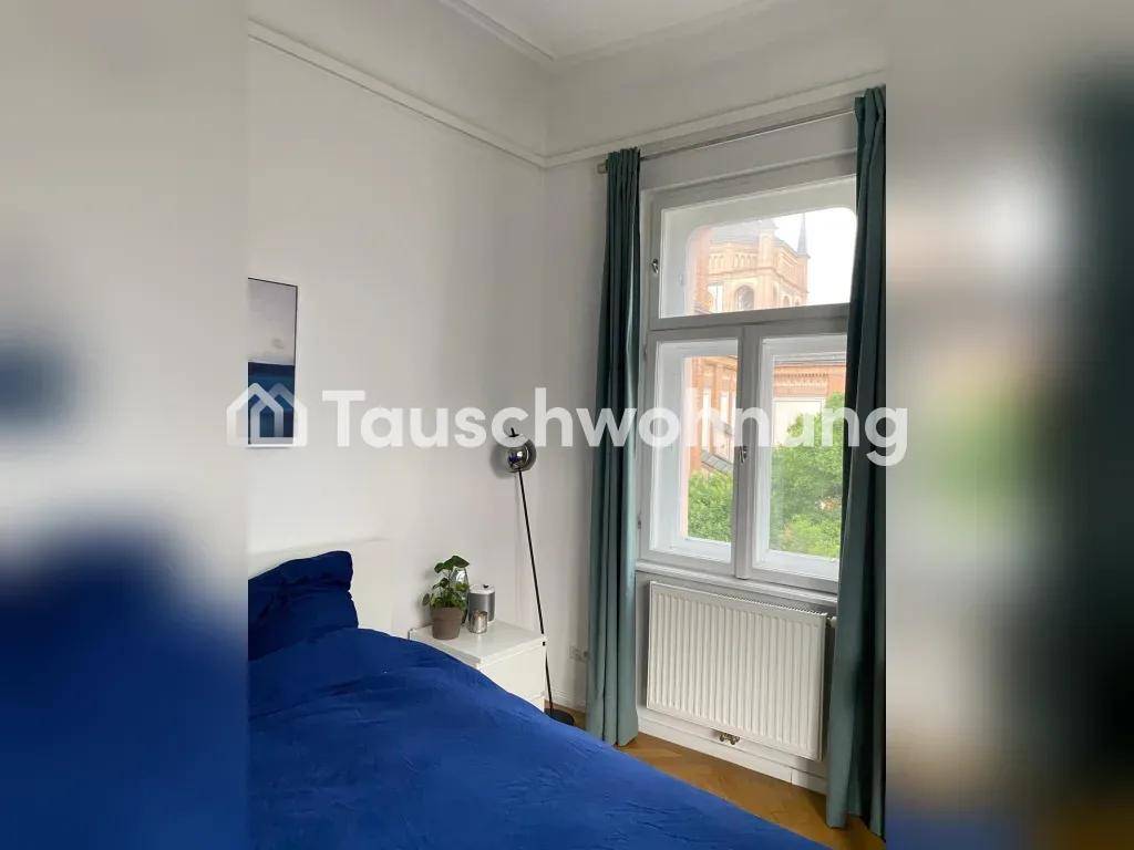 Helles Schlafzimmer mit blauem Bett, Nachttisch und Blick auf ein historisches Gebäude.