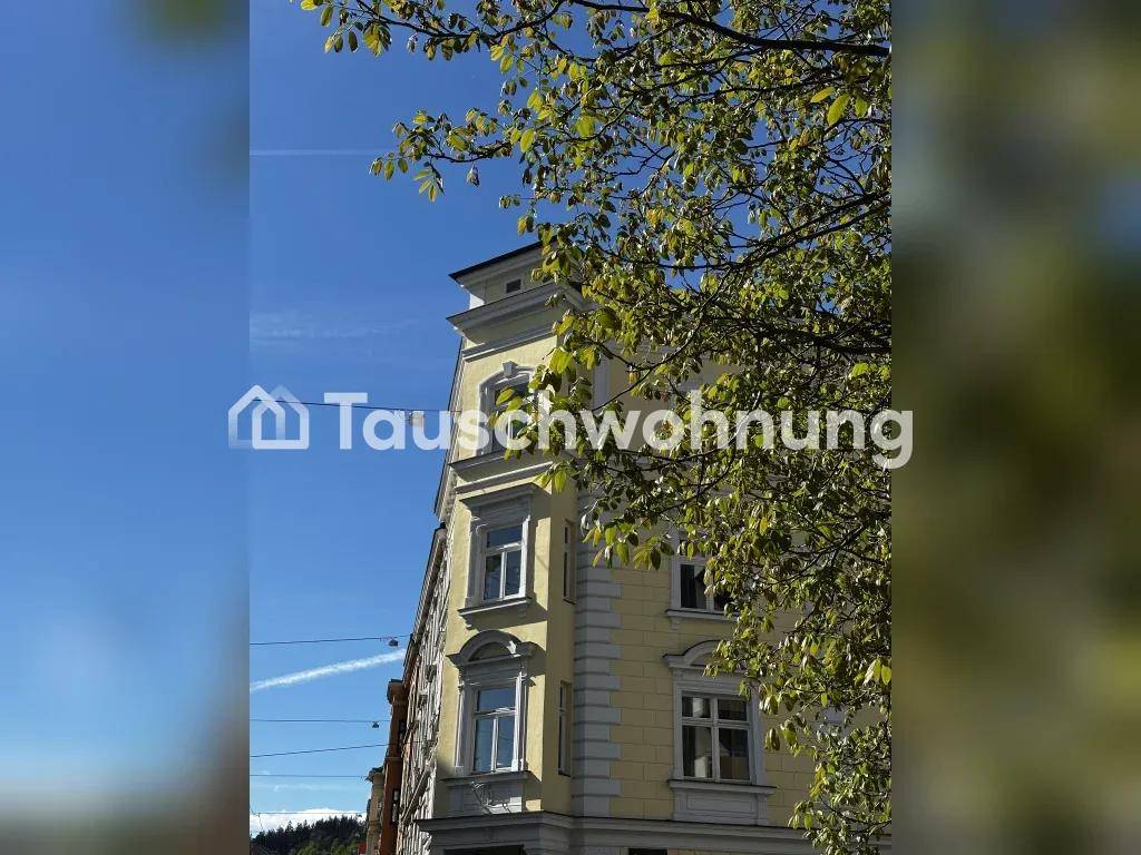 Historisches Gebäude mit gelber Fassade und weißen Fenstern unter blauem Himmel, umgeben von Bäumen.