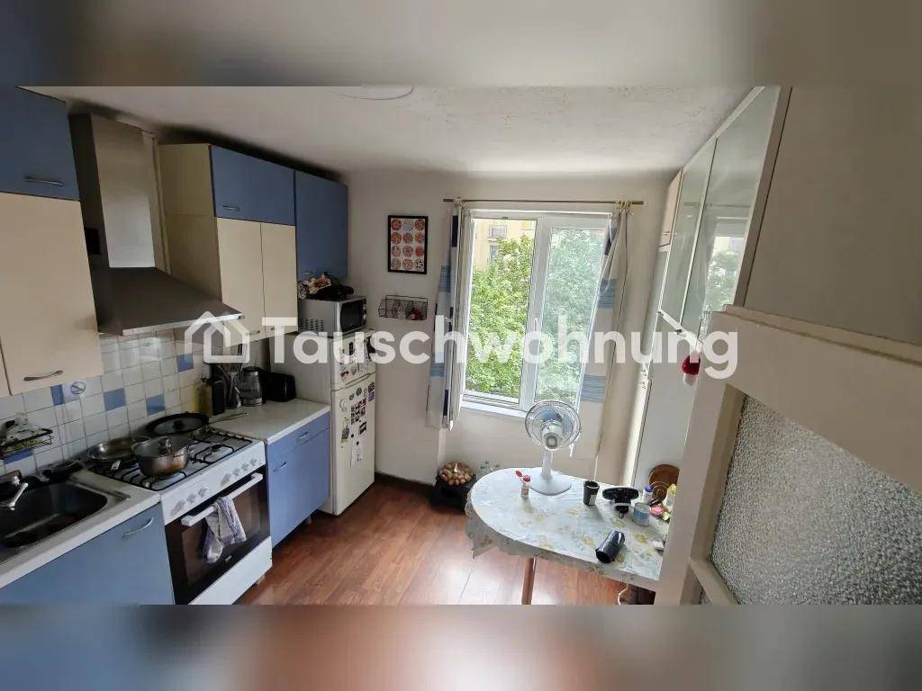 Kleine Küche mit blauen und beigen Schränken, Gasherd und Fenster mit Blick ins Grüne.