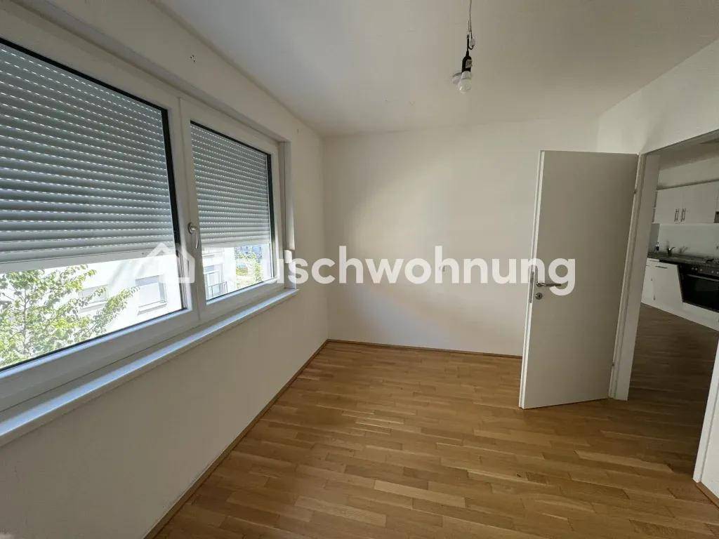 Heller Raum mit Holzfußboden und zwei Fenstern mit Rollläden, bietet Zugang zu einem weiteren Zimmer.