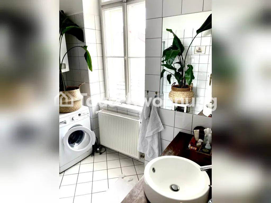Helles Badezimmer mit weißen Fliesen, Waschbecken, Waschmaschine und Fenster.