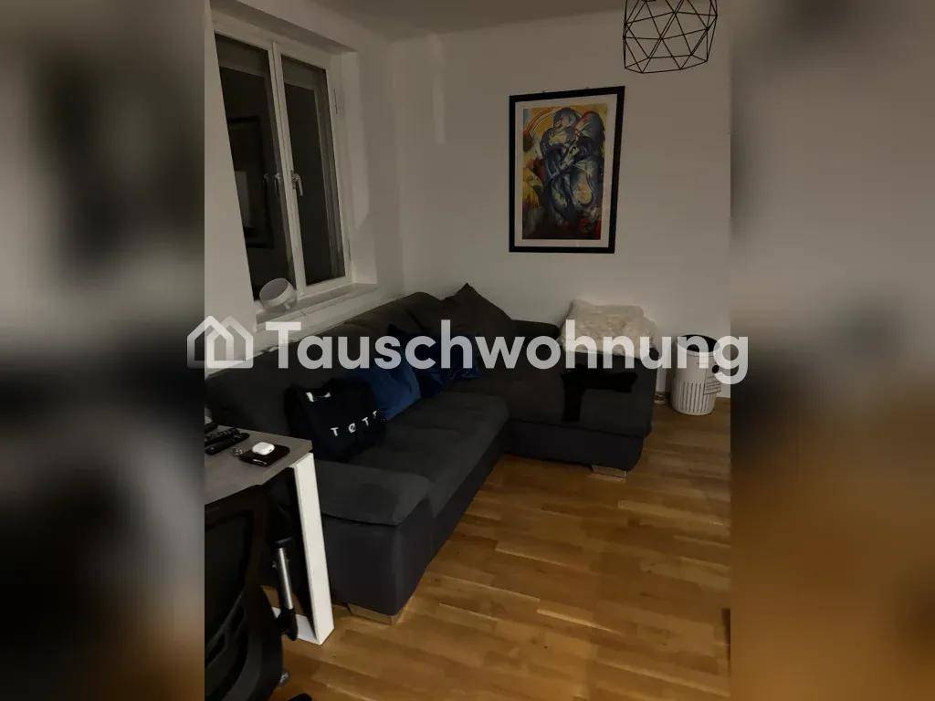 Gemütliches Wohnzimmer mit dunklem Ecksofa, Holzboden und einem Fenster mit Kunstwerk an der Wand.