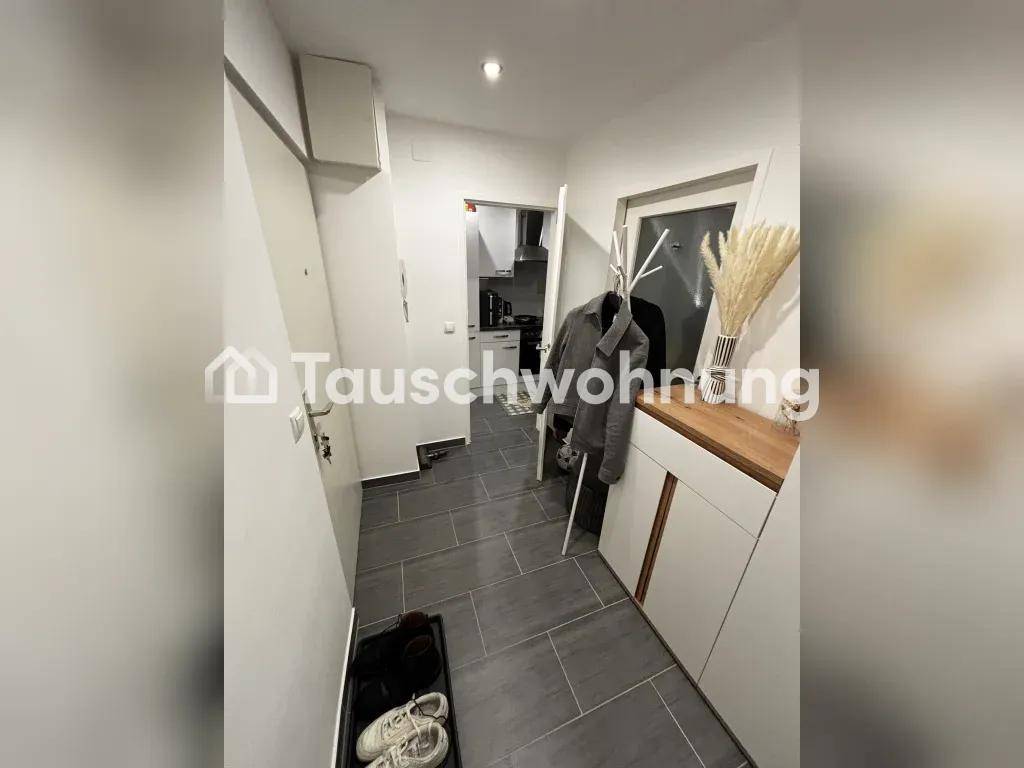 Heller Flur mit grauen Fliesen, Garderobe und Schuhablage, der zu weiteren Räumen führt.