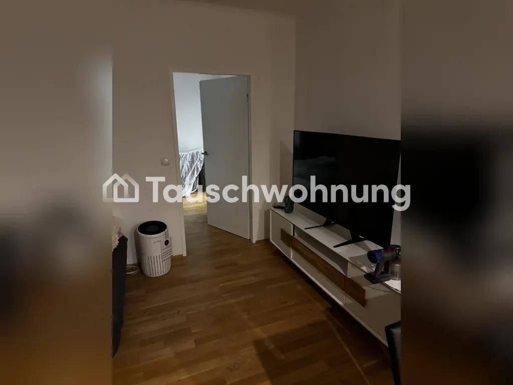 Wohnzimmer mit Fernseher auf einem Sideboard, Holzboden und offener Tür zu einem weiteren Raum.
