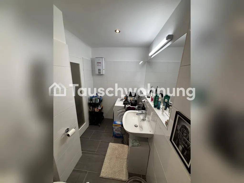 Badezimmer mit weißen Wandfliesen, grauen Bodenfliesen, Waschbecken und einer Waschmaschine.