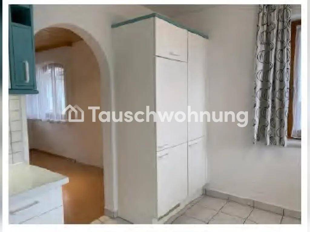 Küchenbereich mit weißen Schränken, Fliesenboden und einem Durchgang zu einem weiteren Raum.
