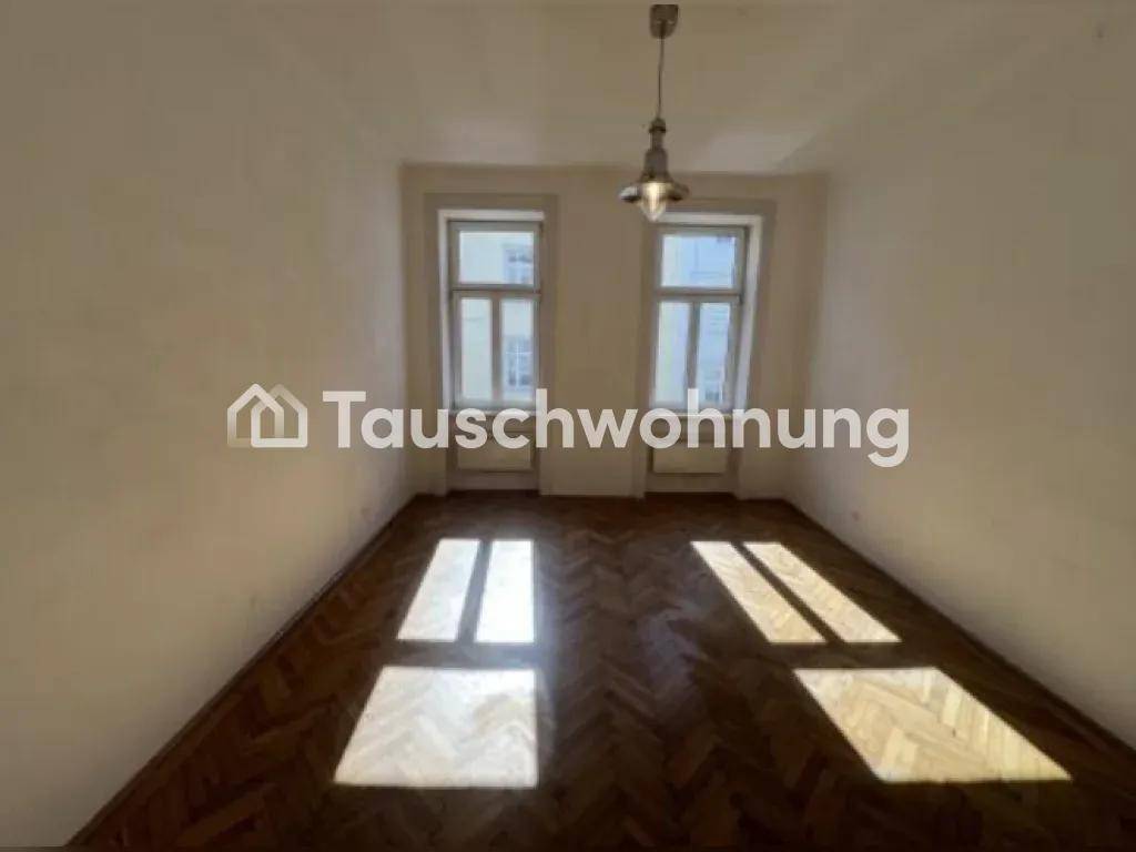 Leeres Zimmer mit Fischgrätparkettboden und zwei großen Fenstern, die viel Licht hereinlassen.