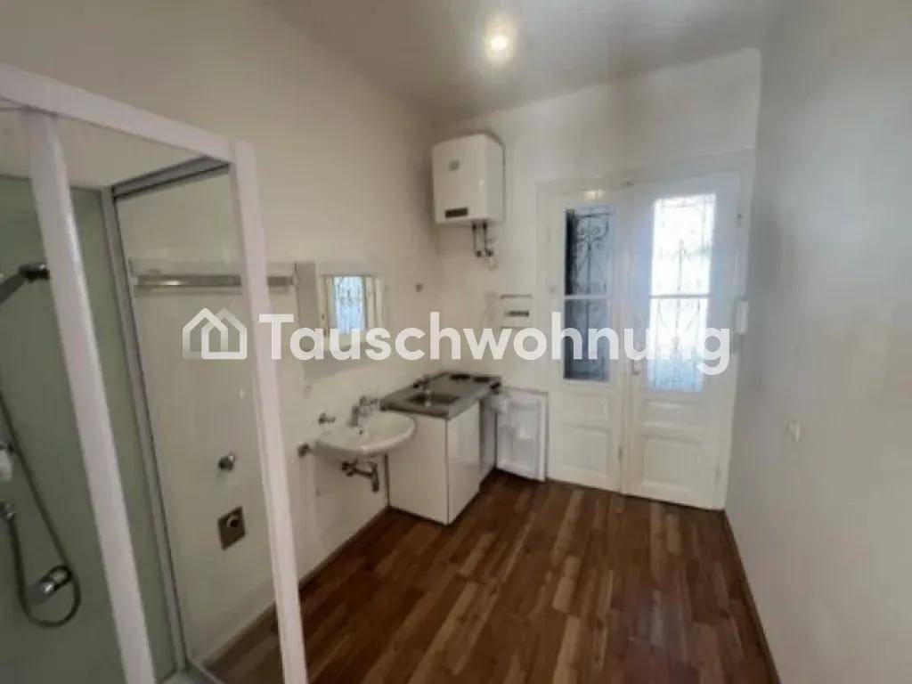 Blick auf die Küchenzeile und Duschkabine in einem hellen Raum mit Holzboden und Tür.