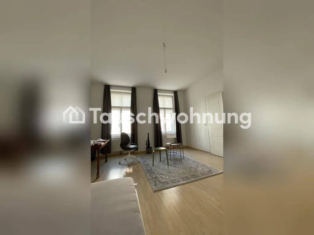 Heller Wohnraum mit Holzboden, zwei Fenstern und schlichten weißen Wänden.