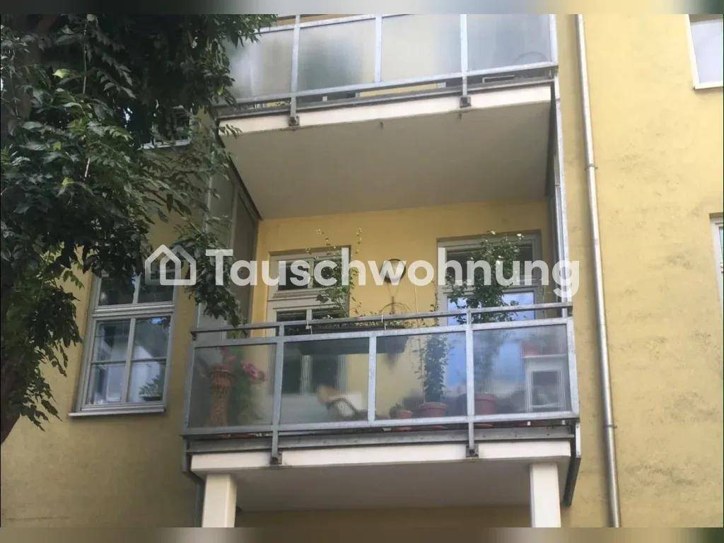 Balkon mit Glasbrüstung und Pflanzen, an einer gelben Gebäudefassade mit Blick ins Grüne.