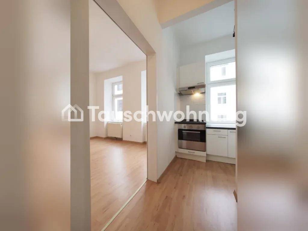 Offener Blick von einem Zimmer in eine kleine Küche mit weißen Schränken und Ofen.