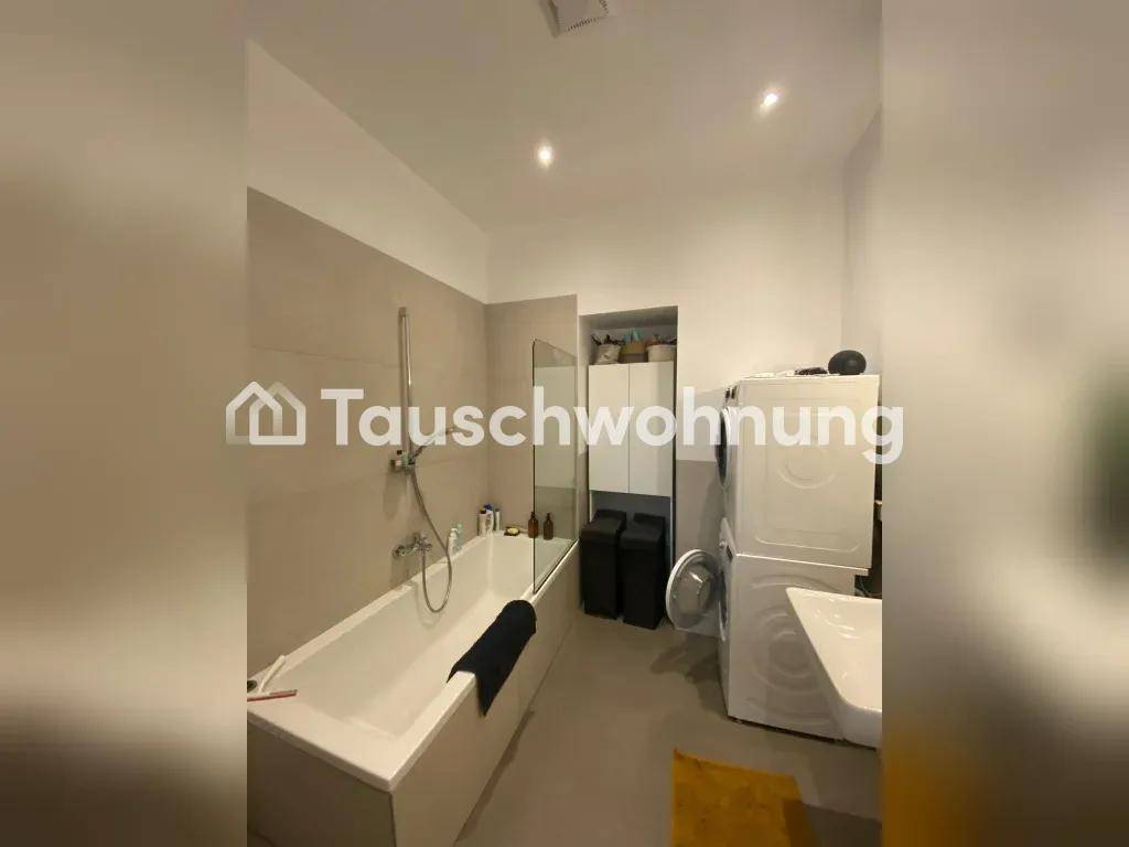 Badezimmer mit Badewanne, Duschvorrichtung und Waschmaschine, in neutralen Fliesenfarben.