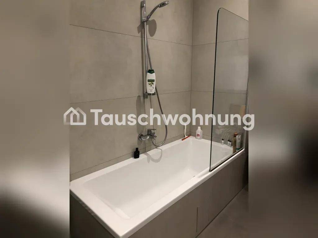 Nahaufnahme einer Badewanne mit Duscharmatur und Glasabtrennung in einem gefliesten Badezimmer.