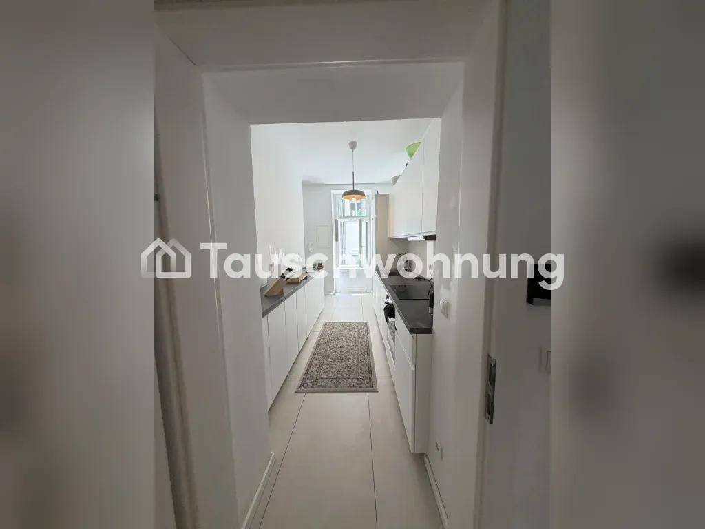 Langer, schmaler Küchenbereich mit weißen Schränken und dunklen Arbeitsplatten, führt zu einem weiteren Raum.