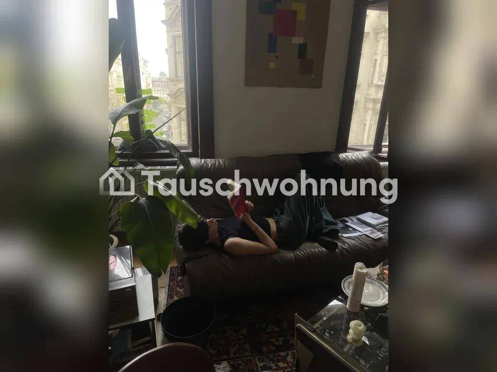 Gemütliches Wohnzimmer mit dunklem Ledersofa, großer Pflanze und Blick auf die Stadt durch die Fenster.