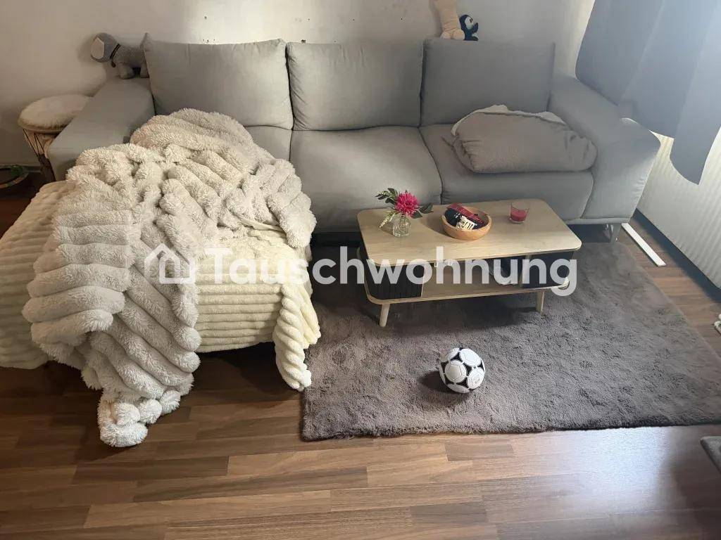 Gemütliches Wohnzimmer mit grauem Sofa, weicher Decke und Teppichboden.
