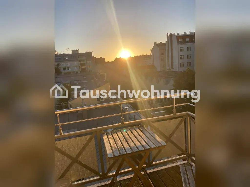 Sonniger Balkon mit Holztisch und Blick über die Dächer bei Sonnenuntergang.