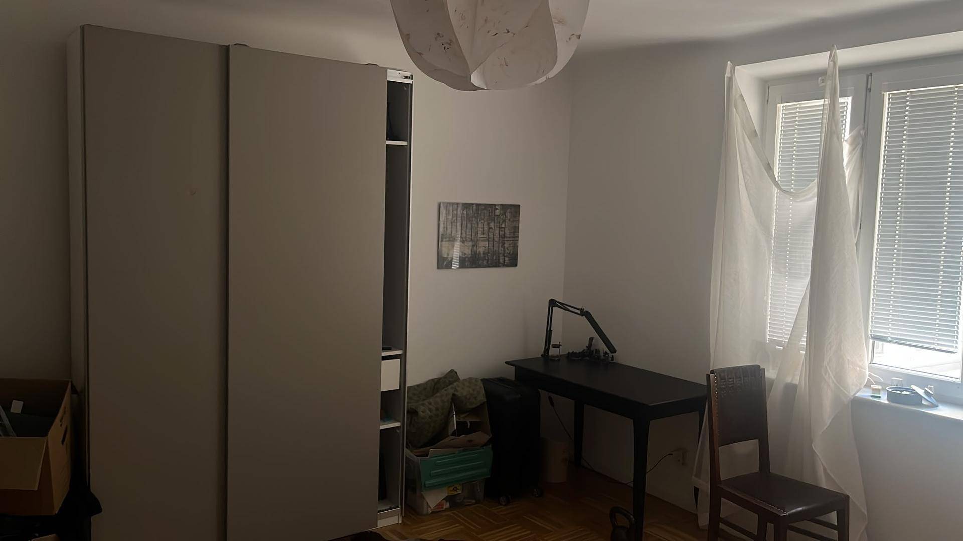 Schlafzimmer mit hellem Parkettboden, einem Kleiderschrank und einem Schreibtisch unter dem Fenster.