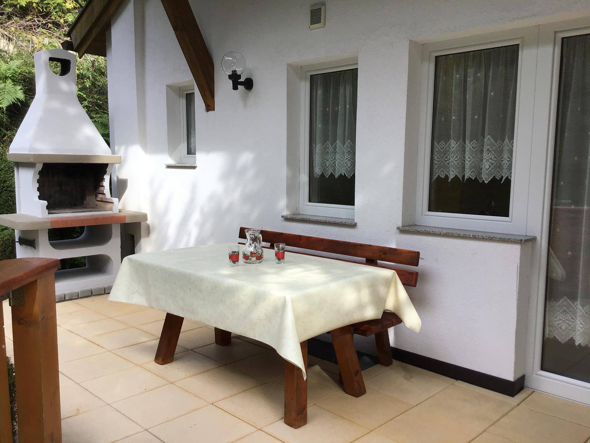 Geflieste Terrasse mit Esstisch, Sitzbank und gemauertem Grill für gesellige Stunden im Freien.