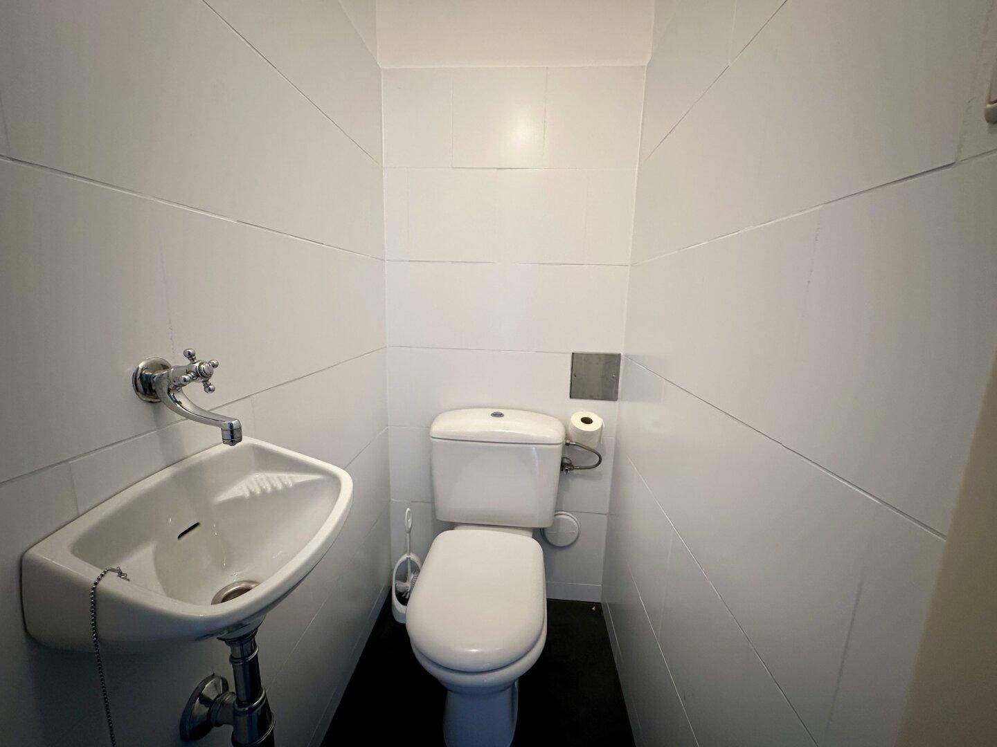 Separates WC mit Waschbecken und weißen Wandfliesen, sauber und funktional.