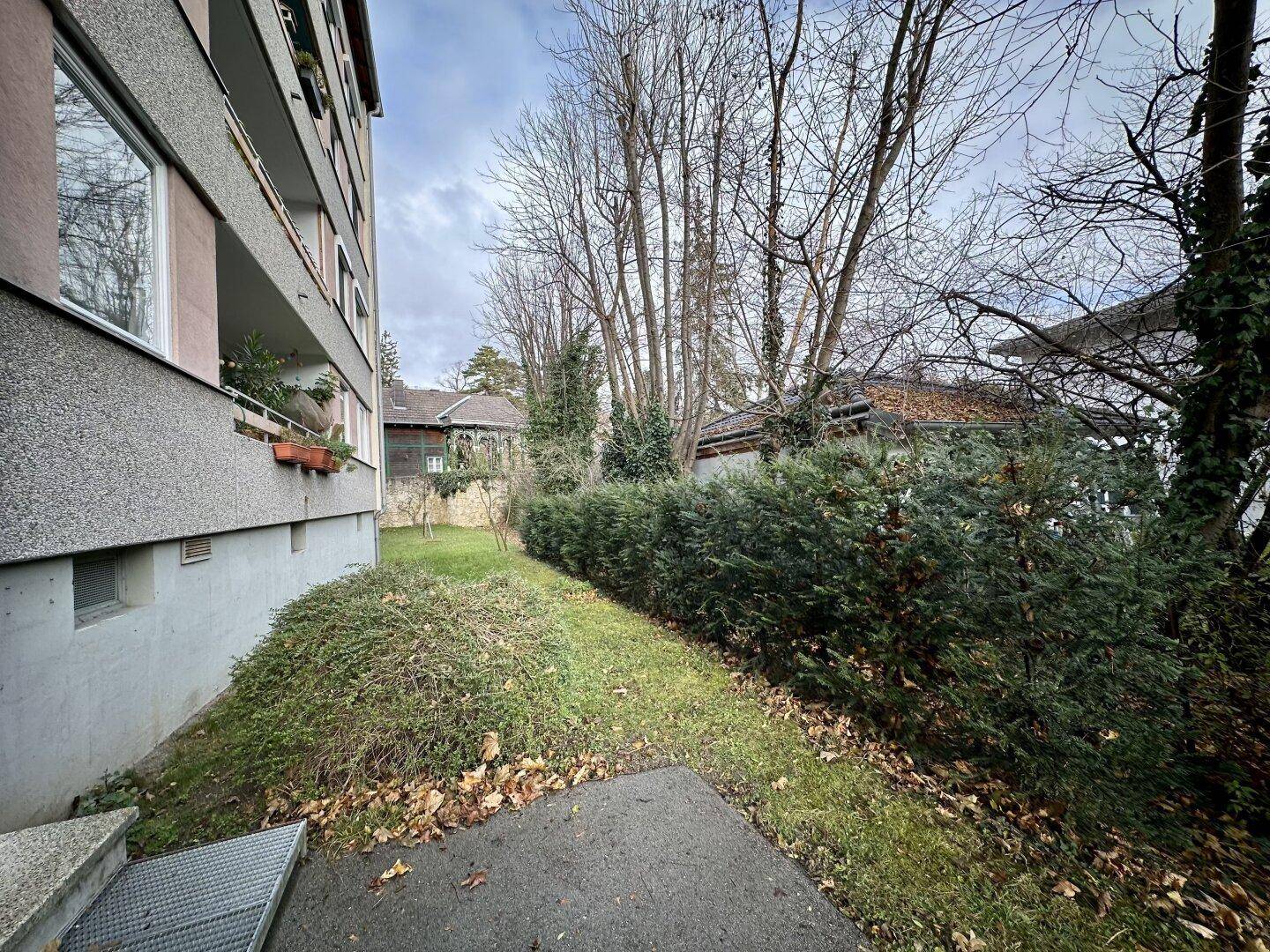 Gepflegter Gartenbereich neben dem Gebäude mit Hecken und Bäumen, ideal zum Entspannen.