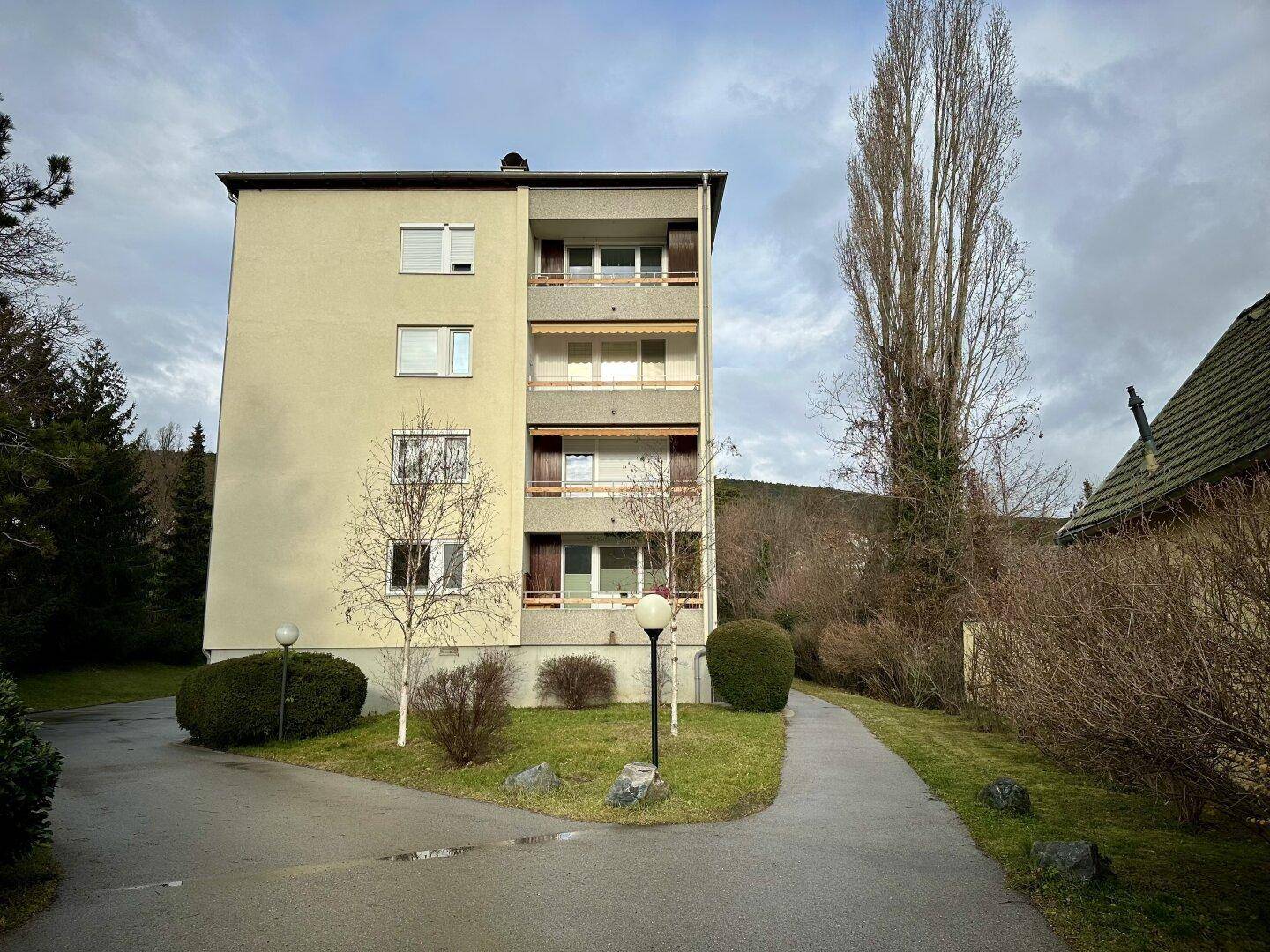Mehrstöckiges Wohngebäude mit Balkonen und grüner Umgebung, umgeben von Bäumen.