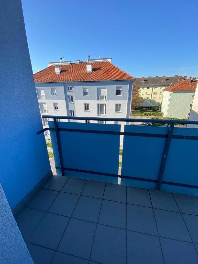 Sonniger Balkon mit blauer Brüstung und Ausblick auf die Nachbarschaft.