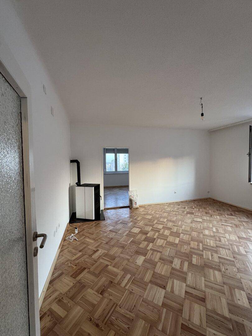 Heller Wohnraum mit Parkettboden und einem modernen Holzofen in der Ecke.
